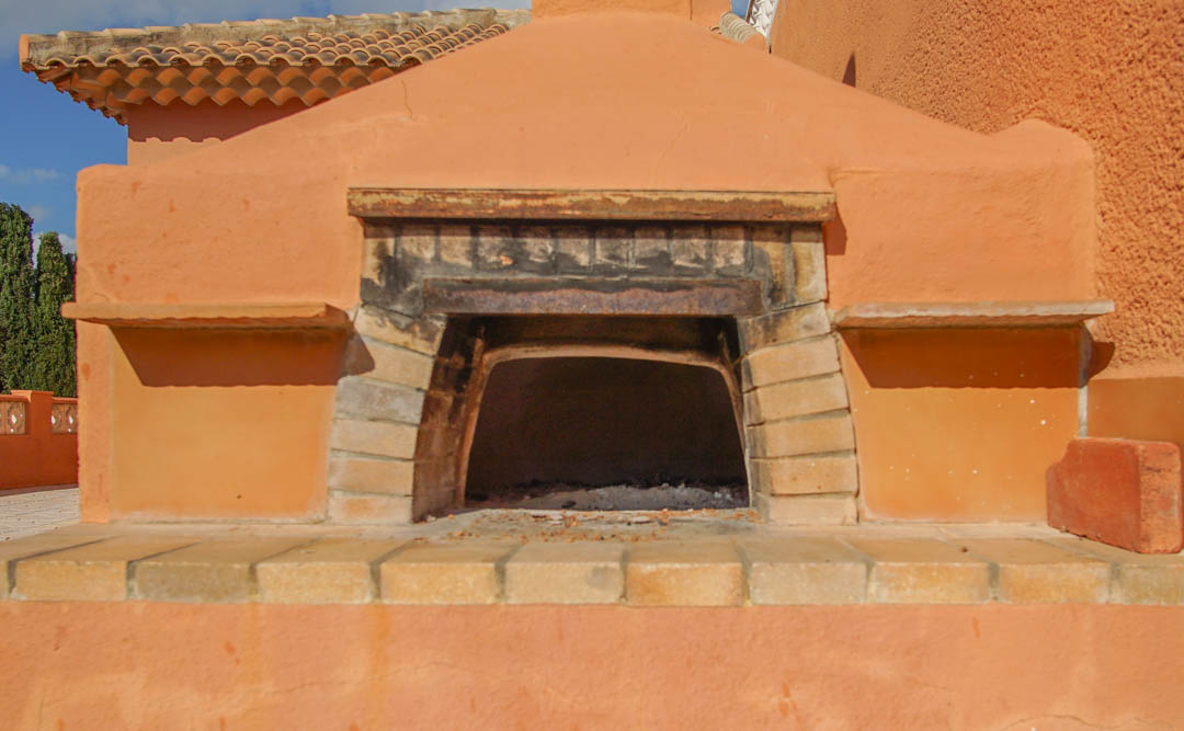 Four à bois extérieur traditionnel intégré dans une structure en maçonnerie terre cuite avec encadrement en briques et toit en tuiles.