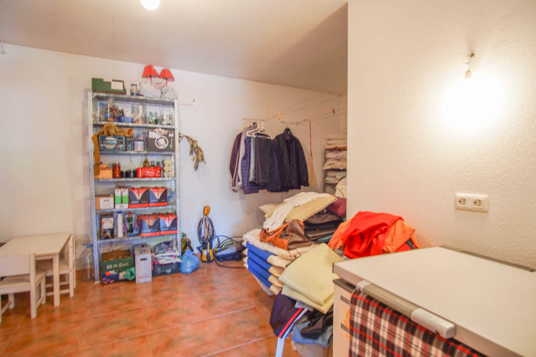 Grand local de rangement au rez-de-chaussée avec sol carrelé, étagères métalliques et espace polyvalent pour l'organisation de la maison.