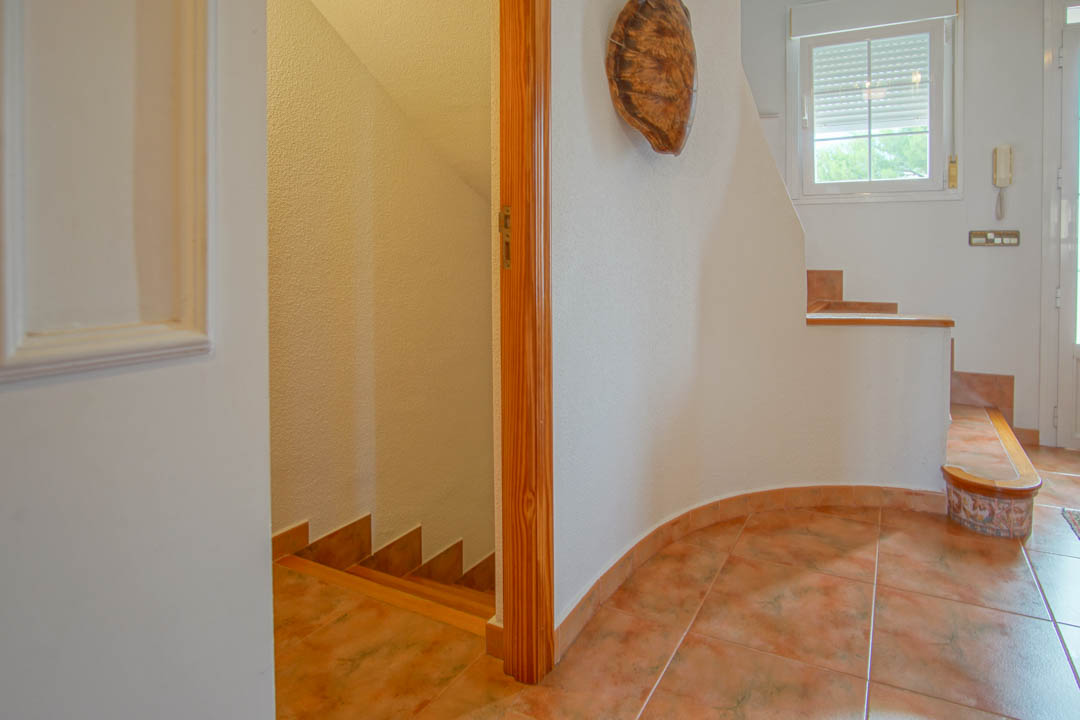 Hall d'entrée avec carrelage en grès et encadrements en bois massif, reliant les étages de la villa par un escalier intérieur central.