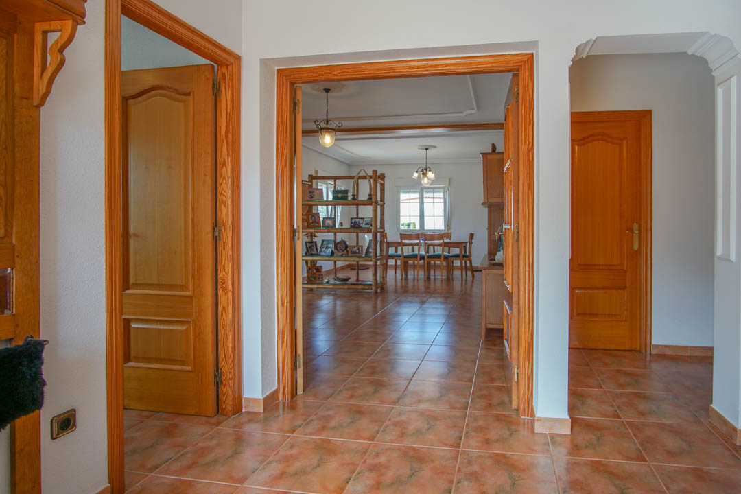 Hall d'entrée avec sol en grès cérame et menuiseries en bois massif ouvrant sur un salon-salle à manger lumineux aux finitions classiques et authentiques.