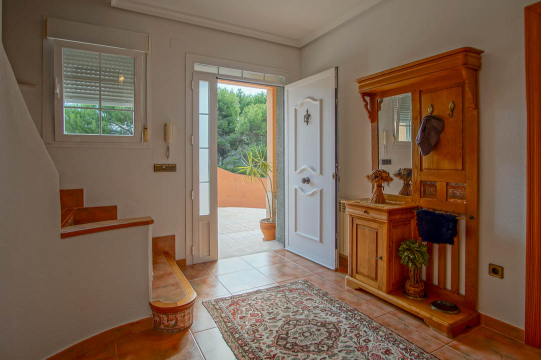 Hall d'entrée avec sol en grès cérame, vestiaire en bois massif avec miroir et porte d'entrée blanche moulurée ouvrant sur l'extérieur.