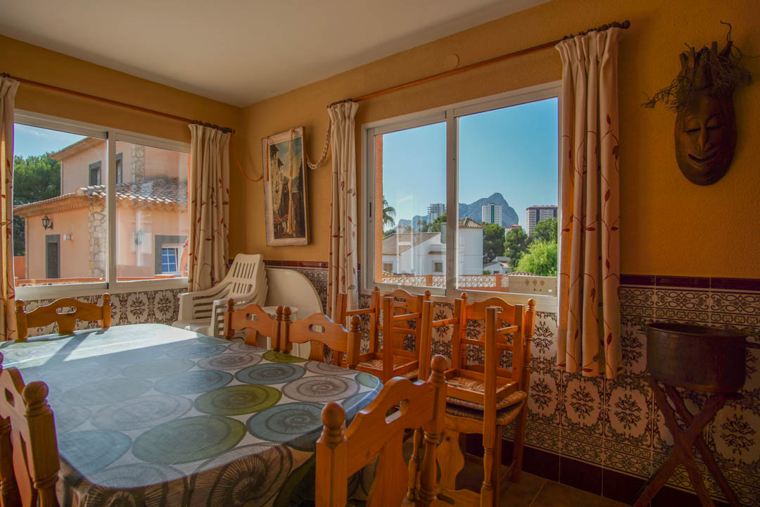 Salle à manger lumineuse avec mobilier en bois massif, soubassement en azulejos traditionnels et fenêtres offrant une vue sur le Peñón de Ifach.