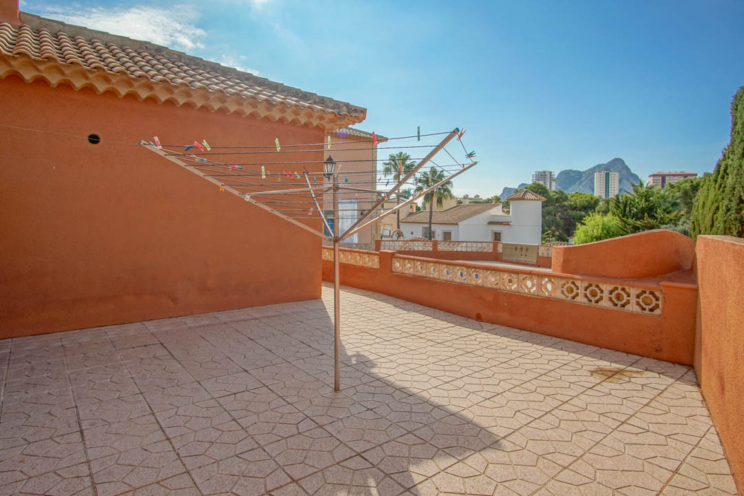 Terrasse solarium avec carrelage à motifs et murs ocre, offrant une vue dégagée sur le Peñón de Ifach et les environs résidentiels.