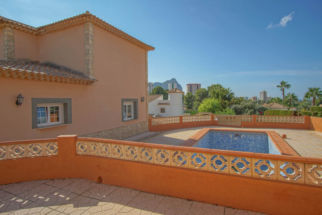 Terrasse surélevée avec piscine privée et balustrade décorative, offrant une vue dégagée sur le Peñón de Ifach et le paysage urbain.
