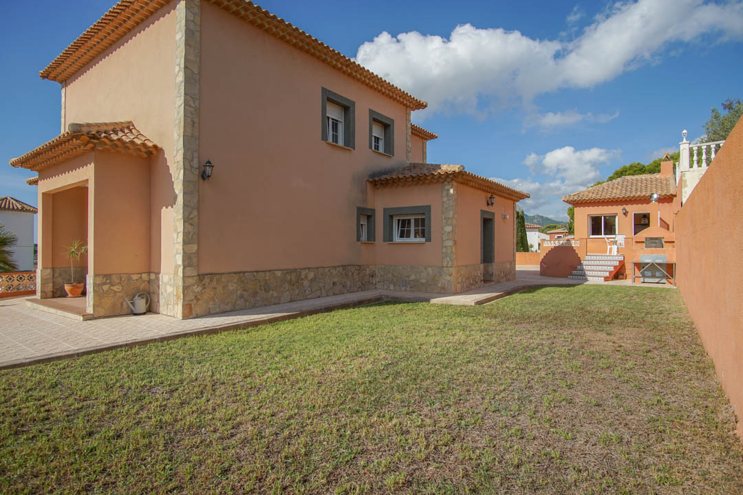 Vue extérieure de la villa avec façade ocre, finitions en pierre naturelle et jardin. Au fond se trouve la cuisine d'été indépendante avec four à bois.