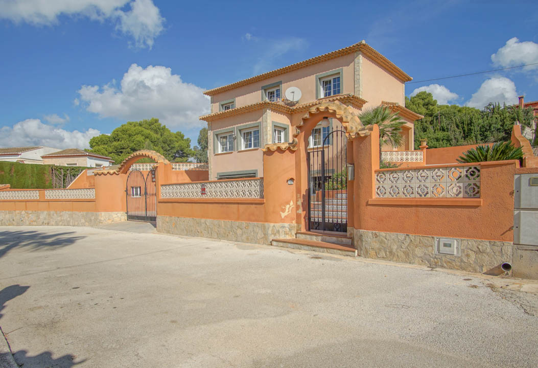 Vue extérieure de la villa sur trois niveaux avec murs terracotta, soubassement en pierre naturelle et portails en fer forgé sous des arches maçonnées.