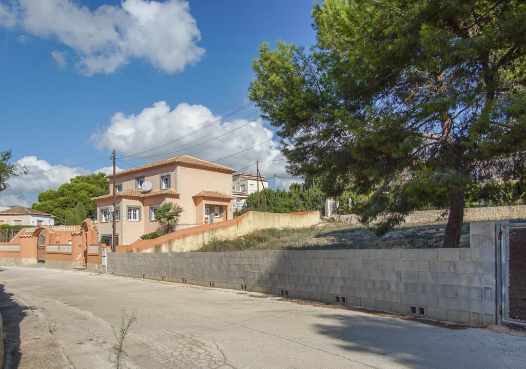 Vue extérieure de la villa sur trois niveaux depuis la rue, présentant le mur d'enceinte, la toiture en tuiles et les pins matures sur le terrain.