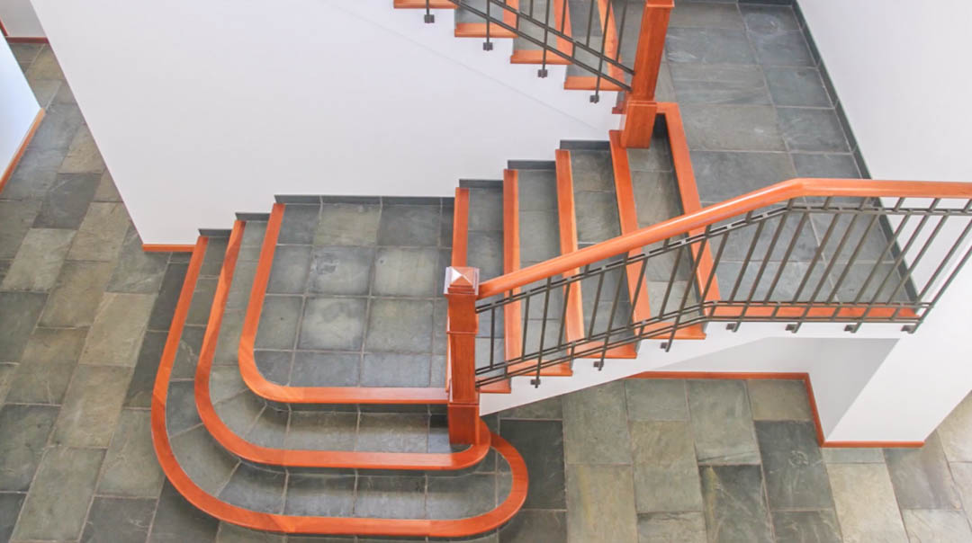 Escalier principal avec marches en pierre naturelle et bordures en bois massif. La rampe en fer forgé et bois souligne le design élégant des sols en dalles sombres.