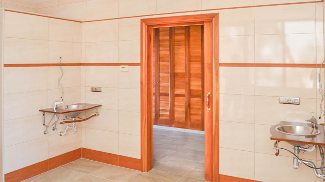 Espace de toilette avec lavabos en acier inoxydable et murs carrelés, ouvrant sur un dressing avec des armoires en bois massif.