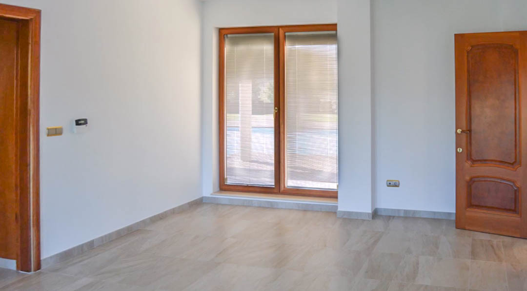 Espace intérieur avec sol en pierre, menuiseries en bois de qualité supérieure et grande fenêtre avec stores intégrés donnant sur la zone de baignade.