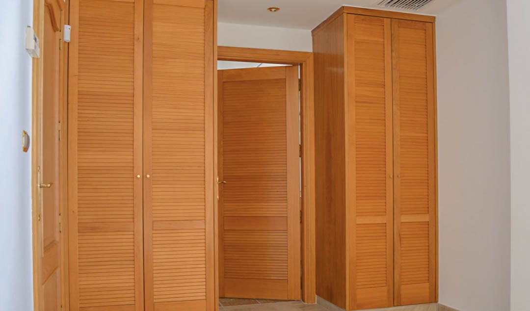 Placards encastrés en bois massif avec portes à persiennes et menuiserie assortie, installés dans un dégagement avec éclairage intégré au plafond.
