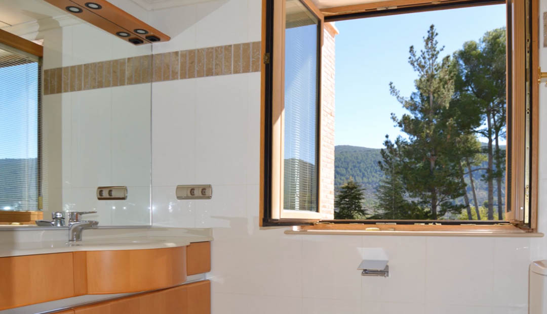 Salle de bain lumineuse avec meuble en bois, vasque intégrée et fenêtre ouverte offrant une vue sur les montagnes et la forêt de pins.