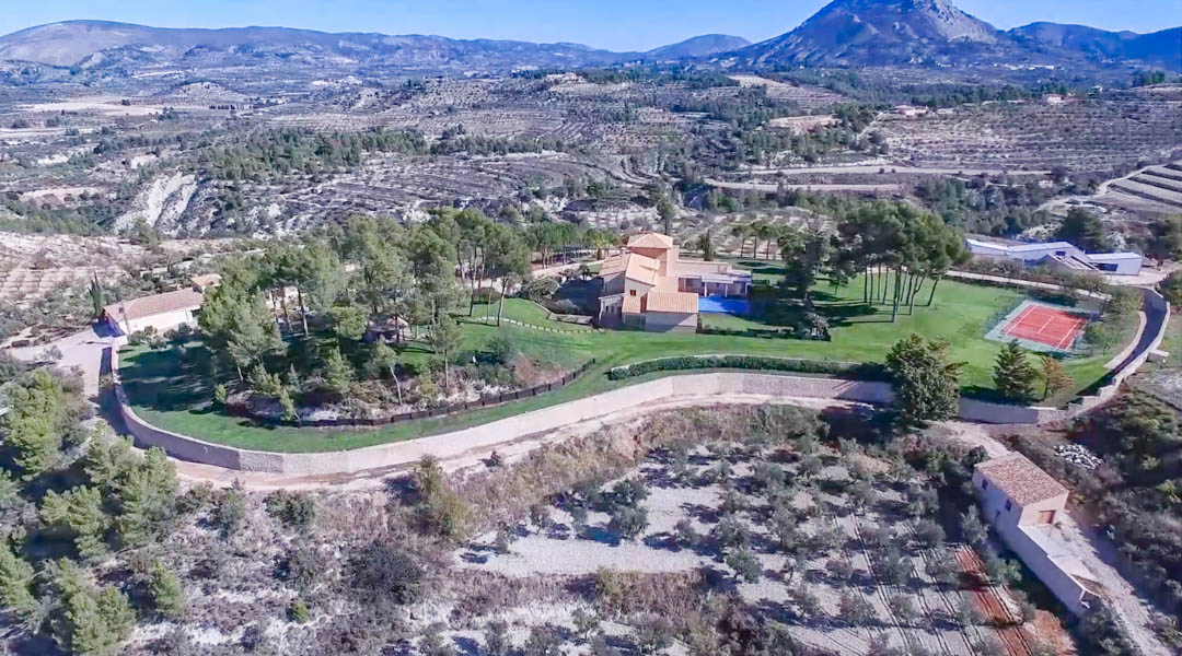 Vue aérienne du domaine présentant la villa principale, la piscine et le court de tennis, entourés de jardins paysagers et de champs en terrasses méditerranéens.