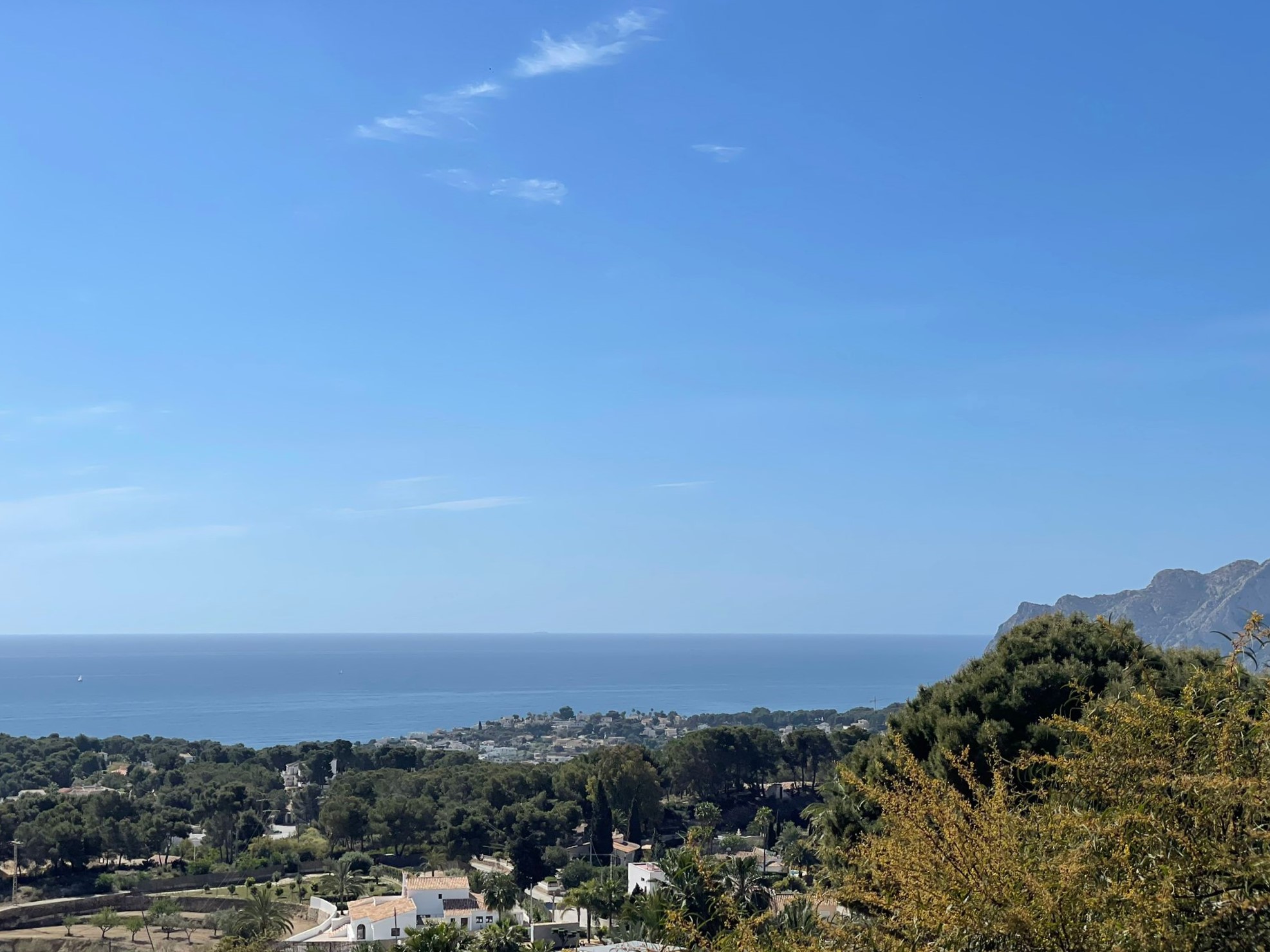 Vue panoramique sur la côte de Benissa, avec la végétation méditerranéenne, des villas résidentielles et la mer sous un ciel dégagé.
