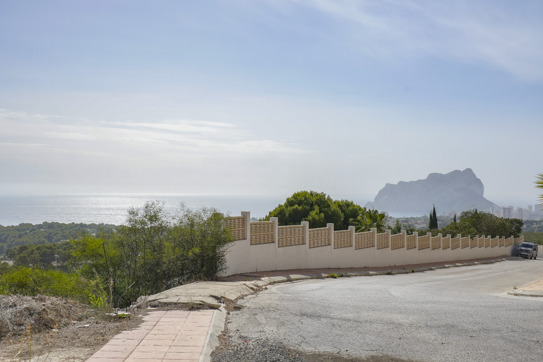 Vue panoramique depuis la rue d'accès, soulignant le mur d'enceinte de la propriété et le Peñón d'Ifach se détachant sur la mer Méditerranée.