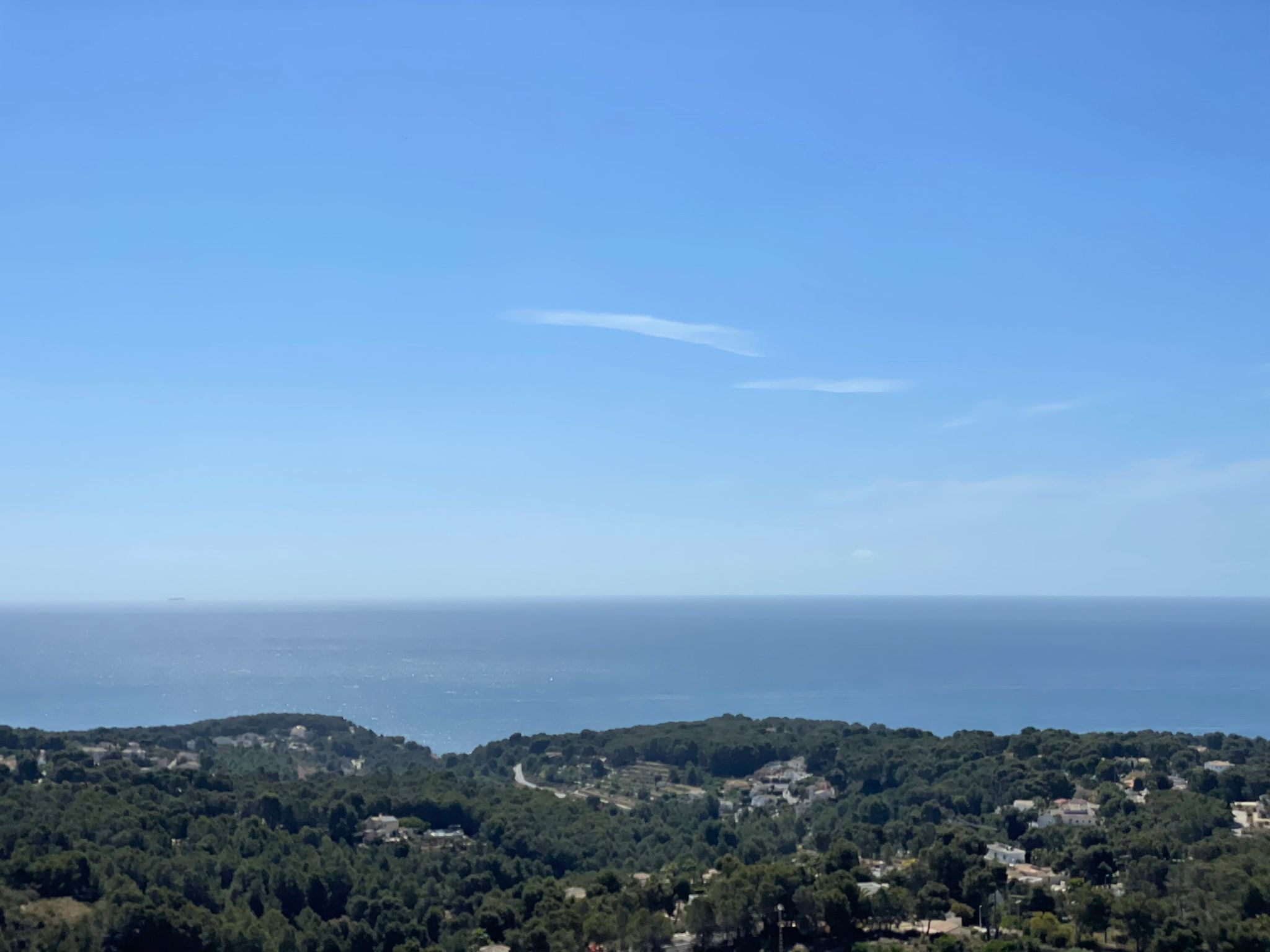 Vue panoramique sur la mer Méditerranée et la côte boisée de Benissa sous un ciel dégagé, soulignant la position surélevée et l'environnement naturel.