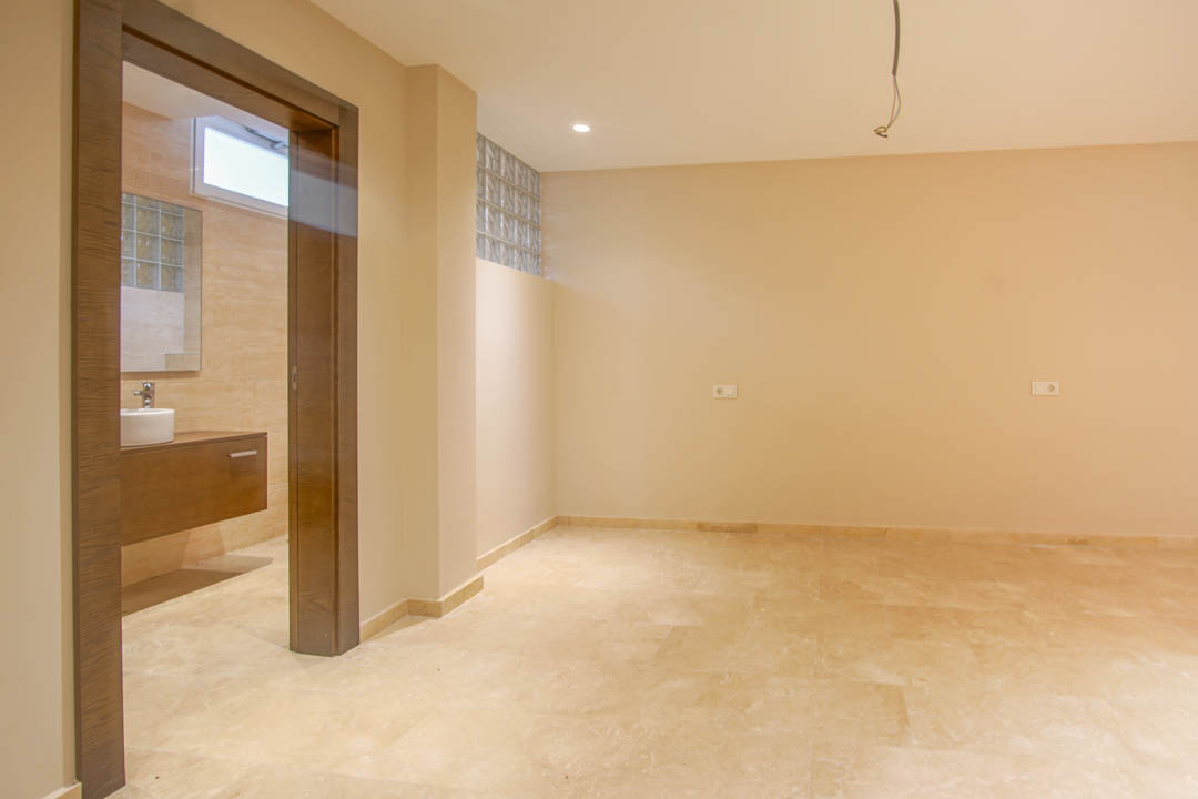 Chambre avec sol en pierre naturelle et salle de bain attenante. Elle dispose d'un meuble vasque suspendu en bois et de briques de verre pour la luminosité.