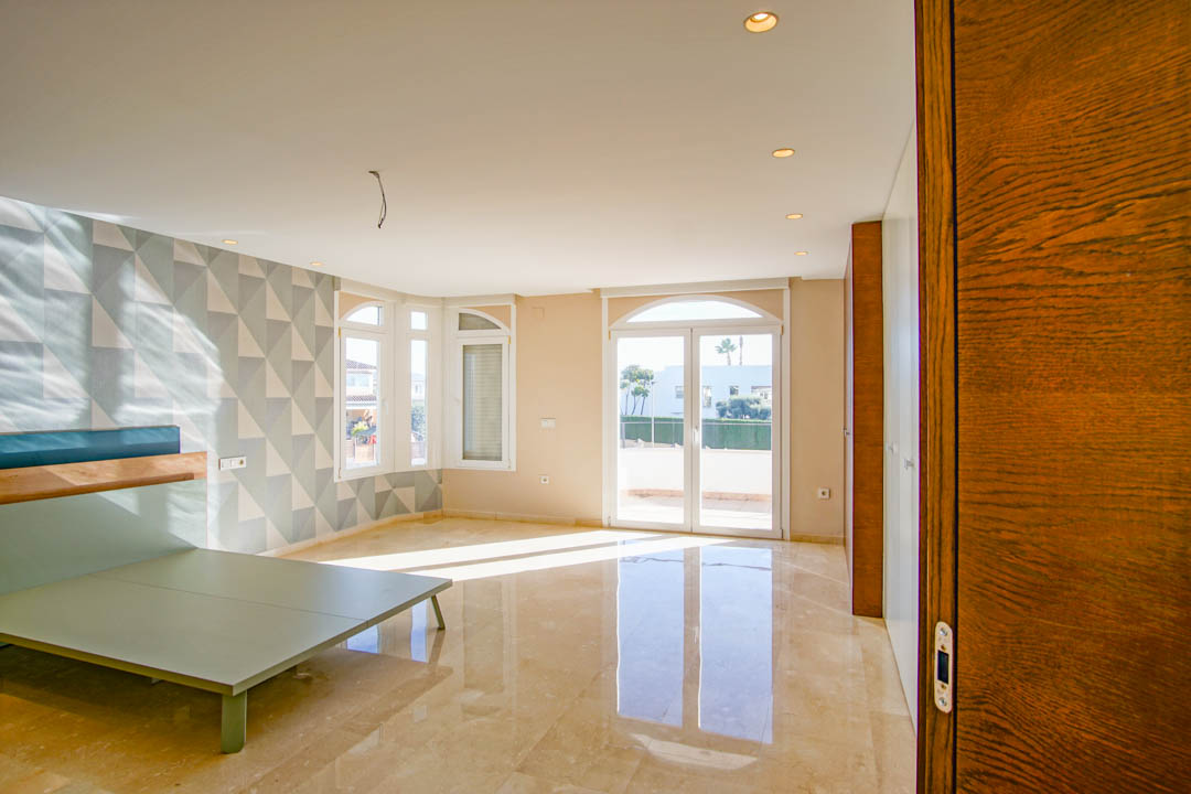 Chambre spacieuse avec sol en marbre poli, mur d'accent au motif géométrique et accès direct à une terrasse ensoleillée par des portes vitrées cintrées.