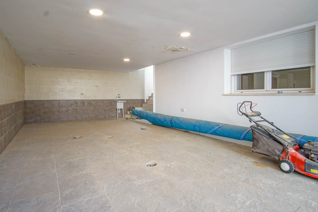 Grand garage avec revêtement de sol en céramique, éclairage encastré et évier utilitaire. L'espace offre un accès direct à l'intérieur et du rangement pour l'équipement.