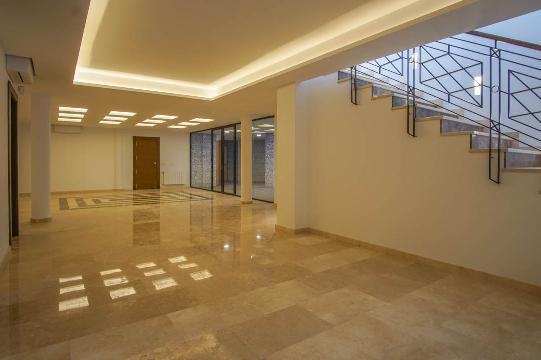 Grand salon au sous-sol avec sols en marbre poli, éclairage LED encastré et cloisons vitrées menant à l'espace bien-être.