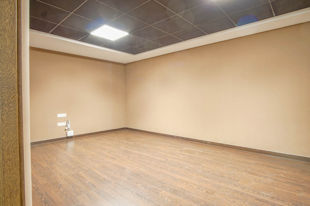 Pièce polyvalente au sous-sol avec sol imitation bois, murs de couleur beige et faux plafond technique doté d'un éclairage LED encastré.