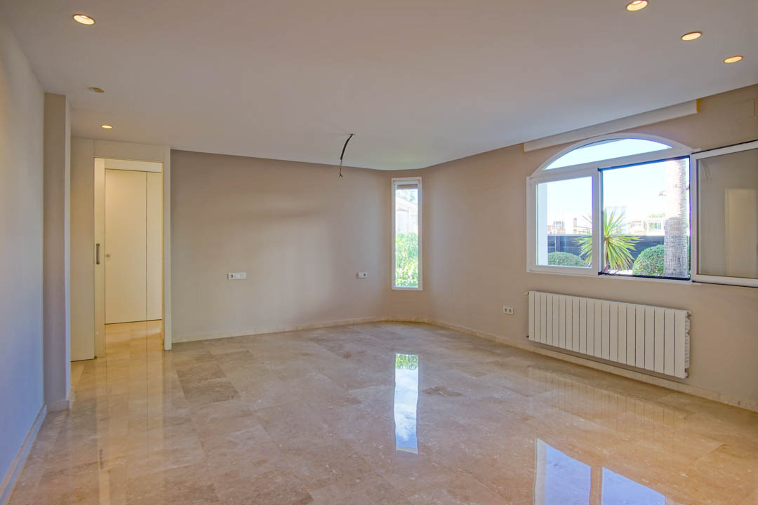 Pièce spacieuse avec sol en marbre poli, spots encastrés et une fenêtre en arc offrant une lumière naturelle et une vue sur le jardin extérieur.