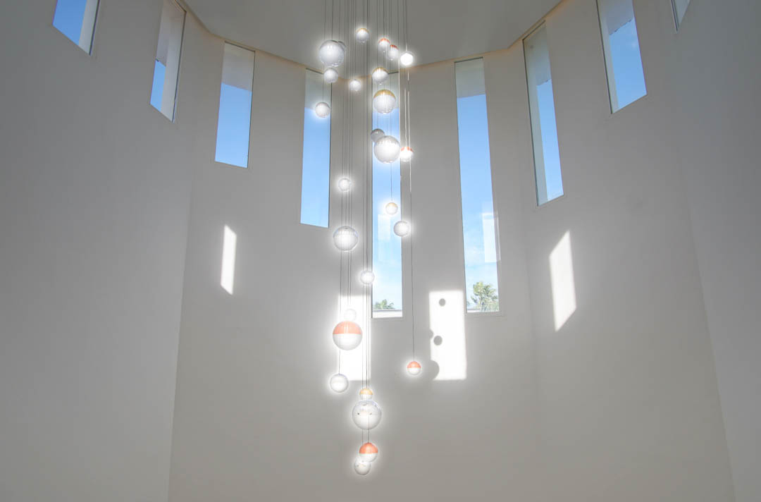 Plafond à double hauteur orné d'un lustre moderne à sphères de verre et de fenêtres verticales étroites laissant entrer une lumière naturelle généreuse.