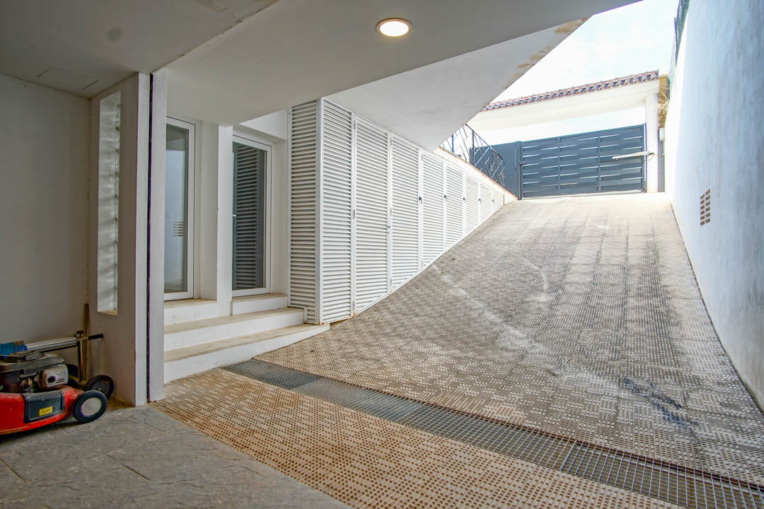 Rampe d'accès au garage avec revêtement antidérapant, rangements à persiennes blanches et entrée secondaire avec portes vitrées.