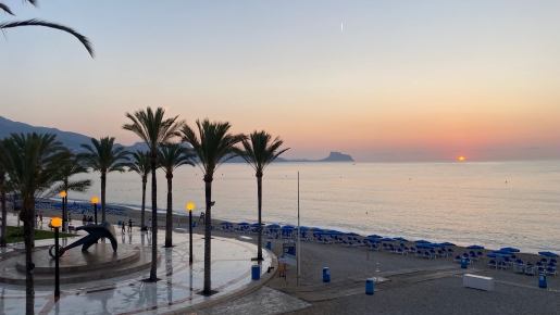 Vue du lever du soleil depuis la promenade maritime avec ses palmiers, sa sculpture d'ancre et sa plage aménagée bordant la mer Méditerranée.