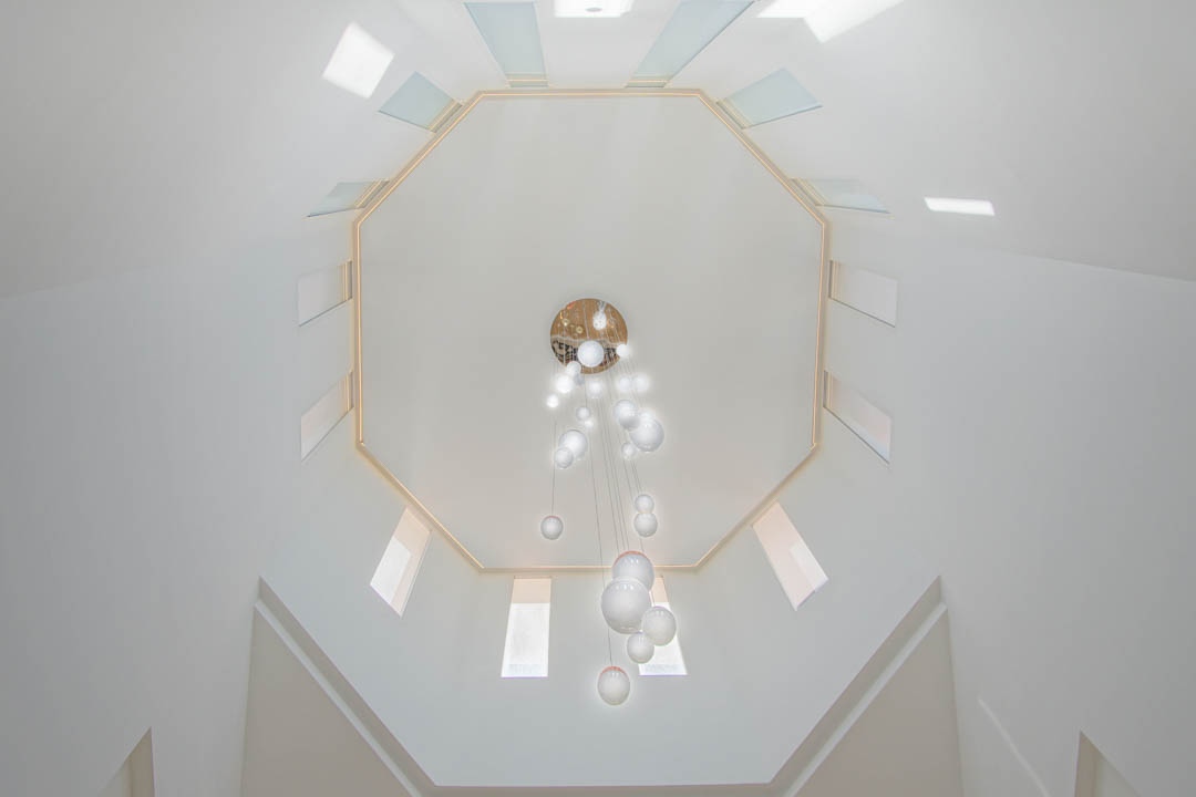 Vue en contre-plongée du plafond octogonal avec puits de lumière symétriques et lustre moderne à sphères de verre dans la cage d'escalier.