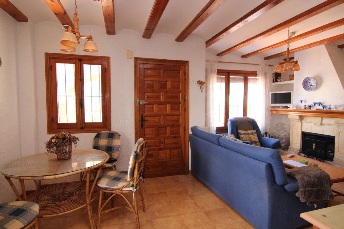 Salon et salle à manger rustiques avec poutres apparentes en bois, sol en grès, cheminée en pierre et mobilier traditionnel sous un éclairage classique.