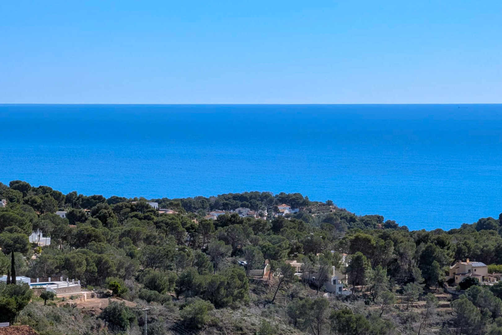 Vue panoramique depuis le terrain sur la mer Méditerranée et les collines boisées de pins de Benissa, avec l'horizon dégagé en arrière-plan.