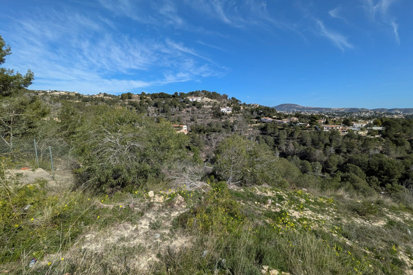 Vue surélevée depuis le terrain escarpé, mettant en valeur la végétation sauvage et les collines boisées de Benissa sous un ciel dégagé.