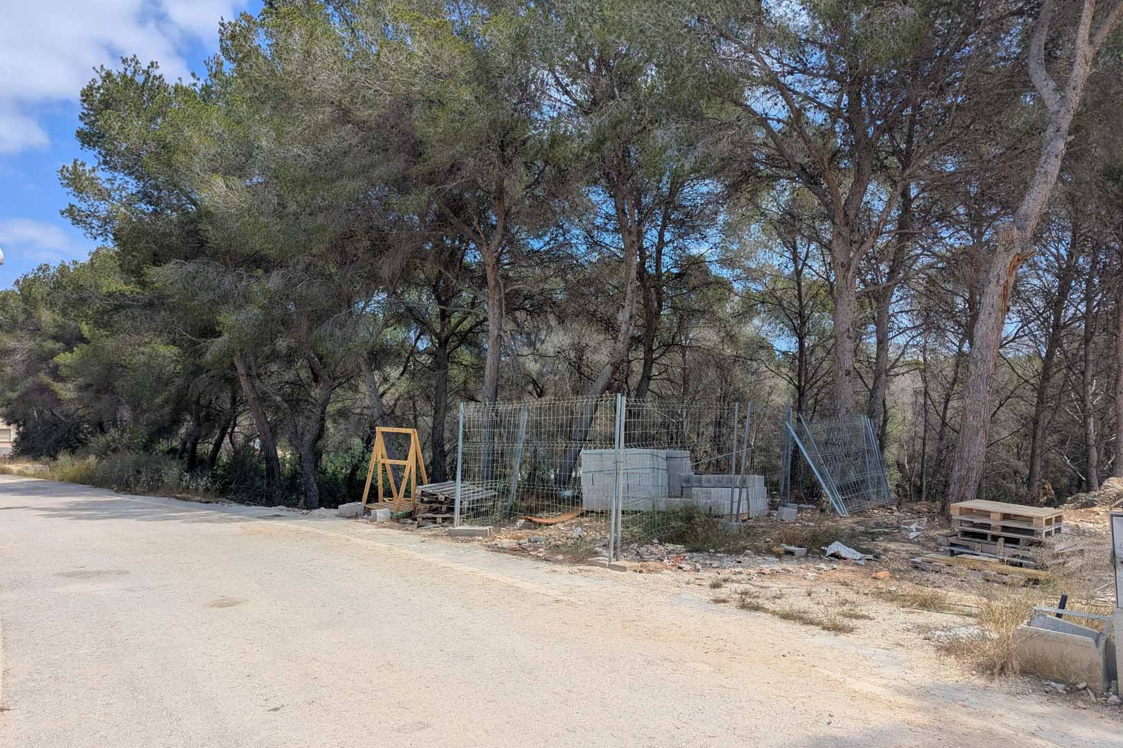 Terrain à bâtir avec pinède naturelle et matériaux de construction initiaux, situé en bordure d'une route asphaltée dans un quartier calme.