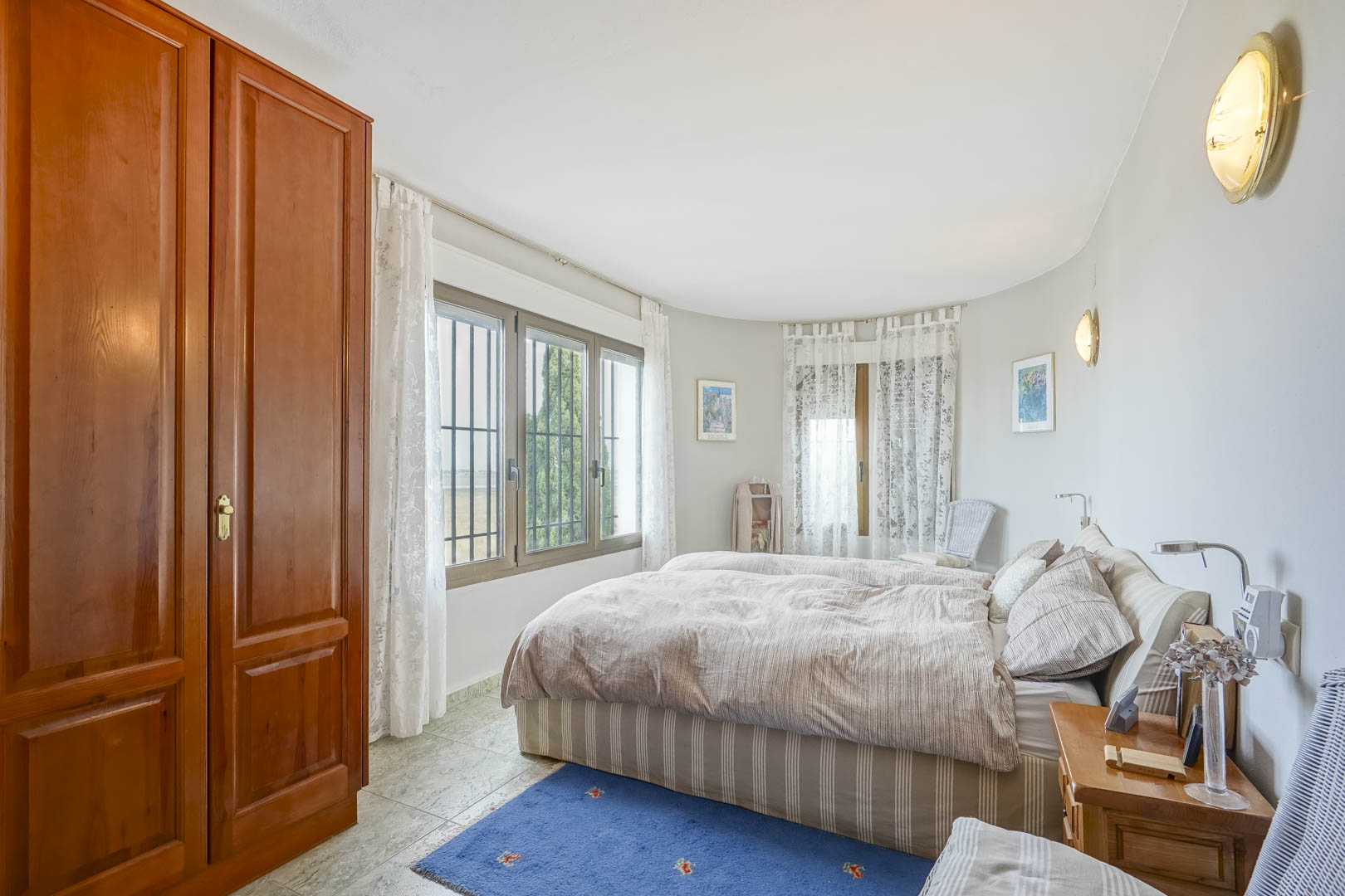 Chambre lumineuse avec armoire en bois, fenêtres panoramiques et literie rayée.