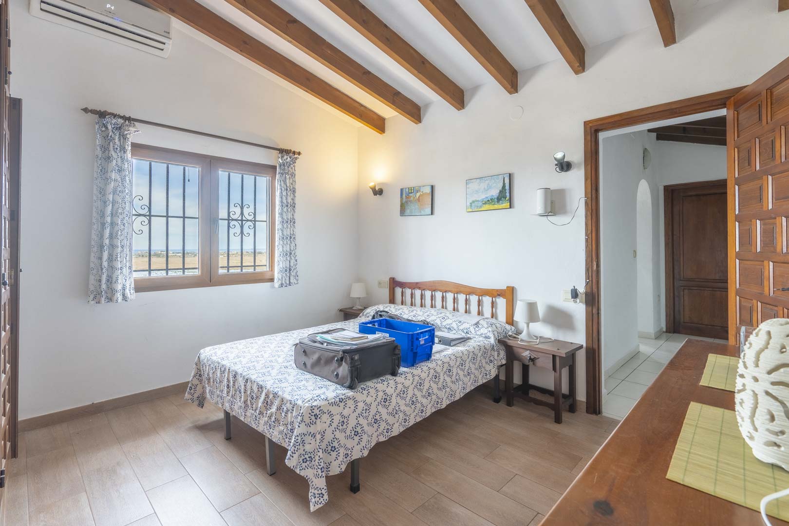 Chambre lumineuse avec poutres apparentes, lit double avec linge de maison à motifs et vue extérieure.