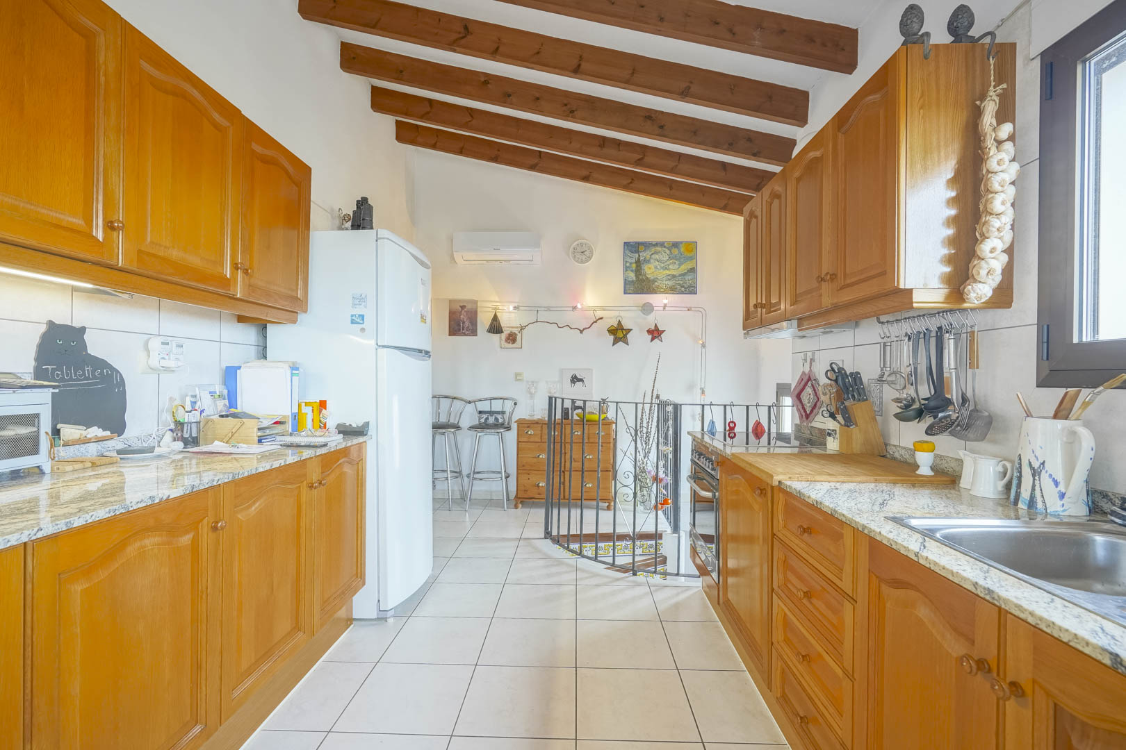 Cuisine ouverte avec poutres en bois, armoires en bois et plans de travail en granit.