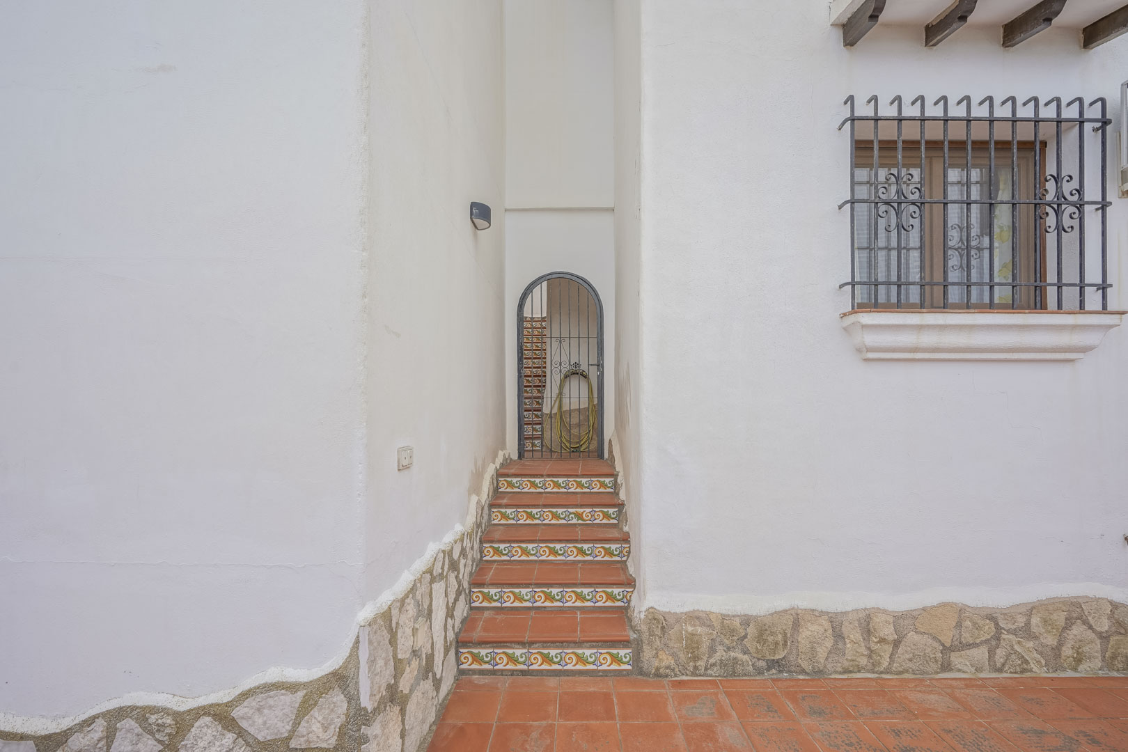 Entrée de la villa avec marches en céramique décorée et portail en fer forgé, détails rustiques sur la façade blanche.