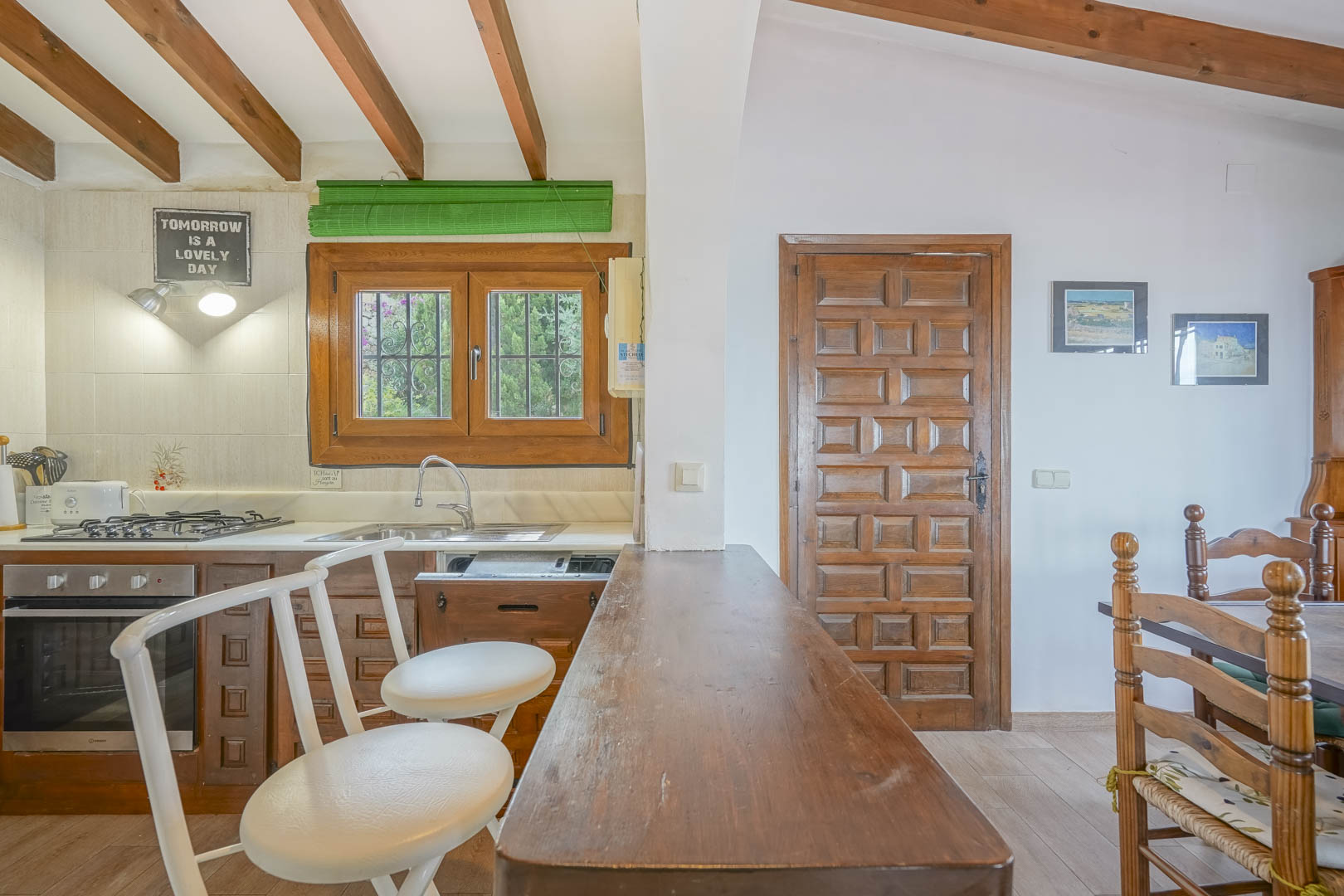 Gros plan sur la cuisine ouverte avec un bar en bois, des tabourets blancs et des poutres apparentes.