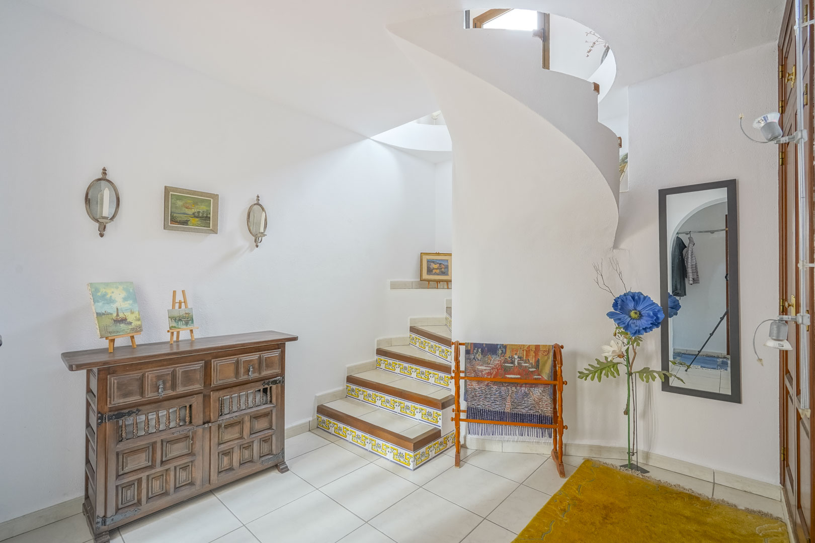 Hall d'entrée lumineux avec escalier en colimaçon et détails rustiques, comme le buffet en bois.