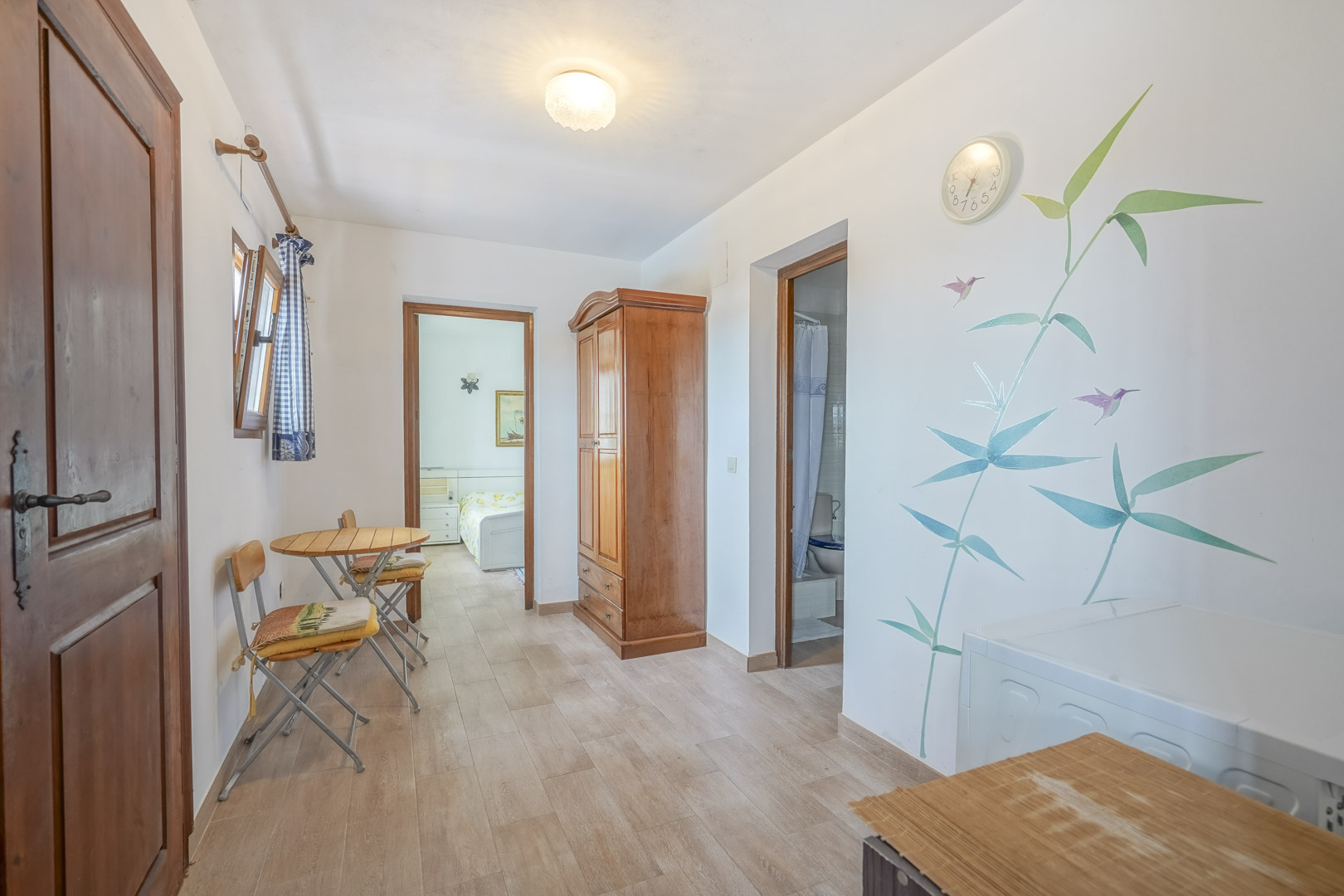 Intérieur lumineux avec carrelage, armoire en bois et décoration murale botanique.