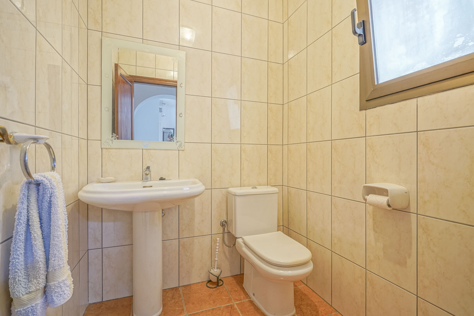 Salle de bain avec carrelage crème, lavabo sur colonne blanc et miroir décoré.