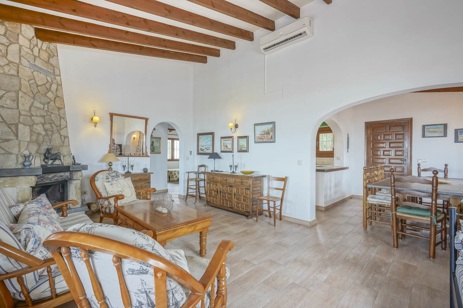 Salon avec cheminée en pierre, poutres apparentes et mobilier rustique. Espaces reliés par des arches.