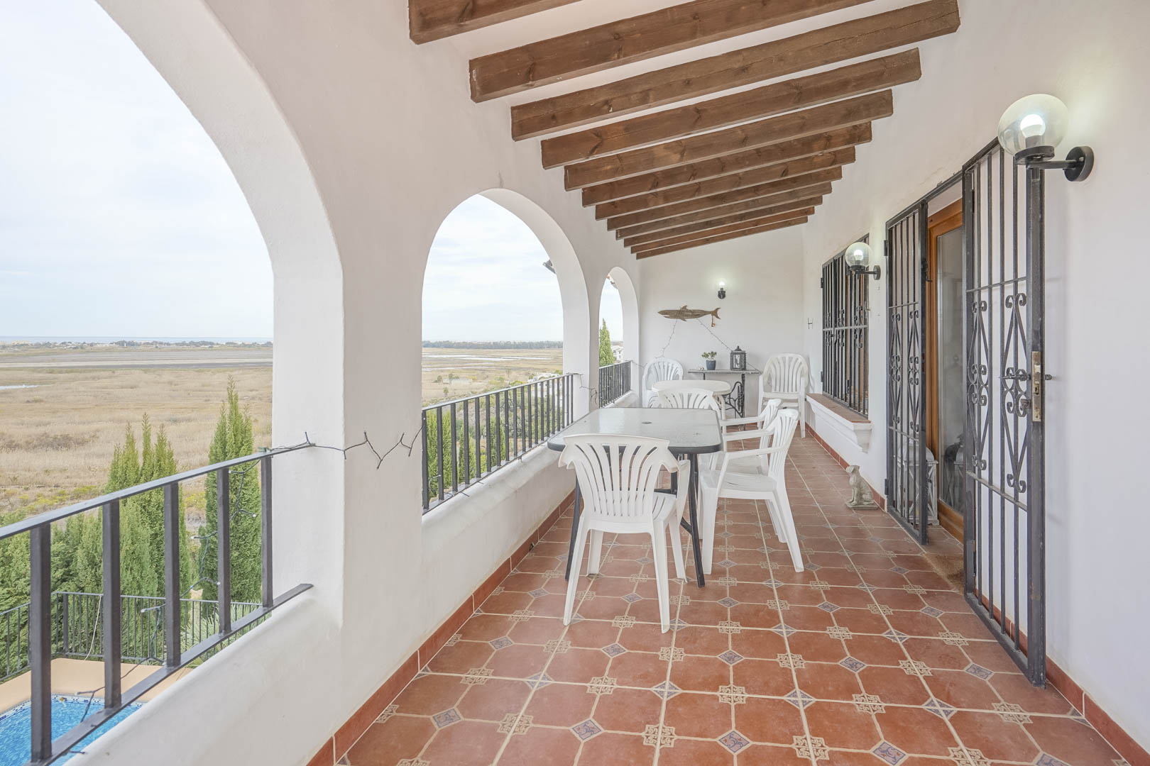 Terrasse couverte avec vue panoramique, arches blanches et sol en carrelage rustique. Mobilier d'extérieur.