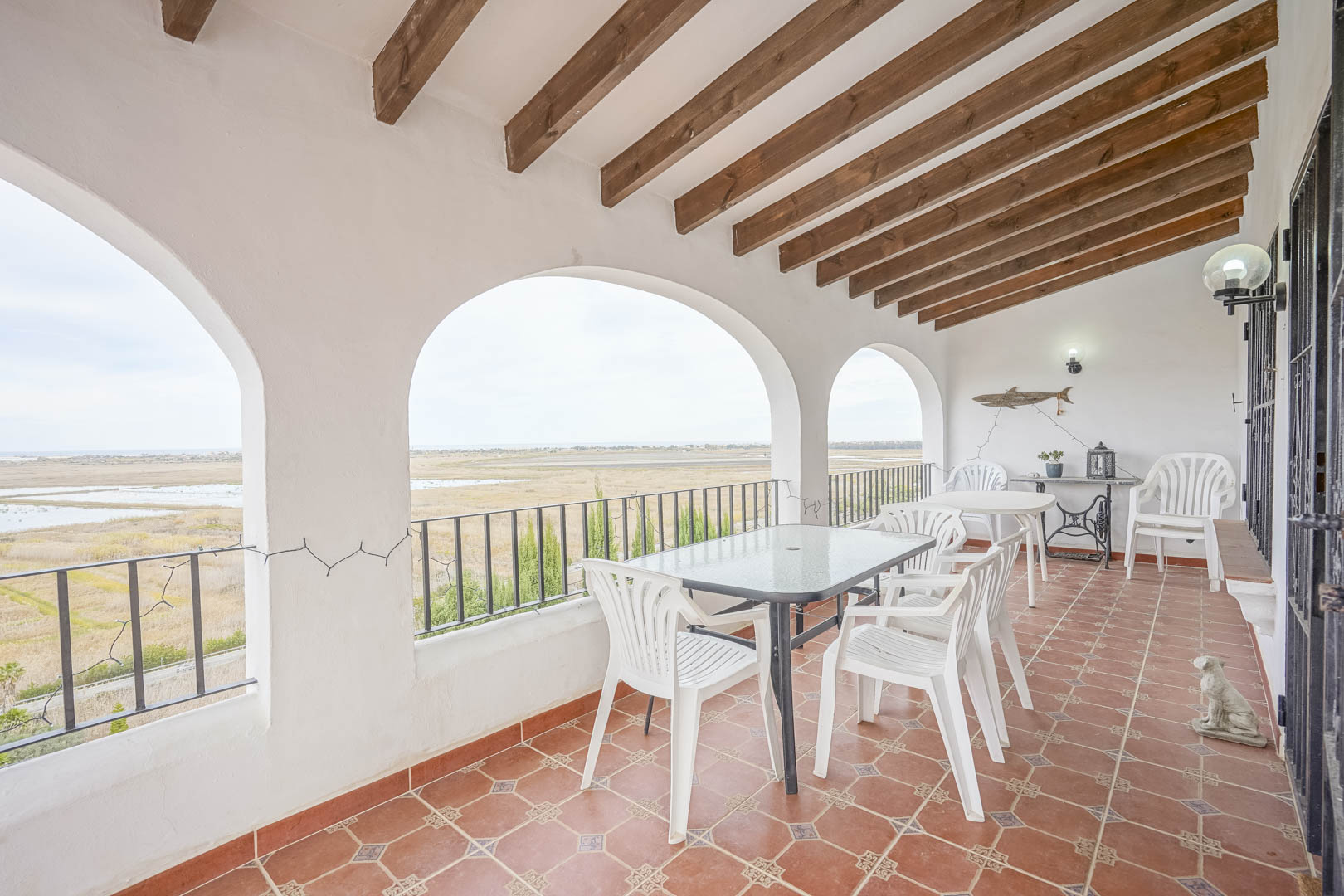 Terrasse couverte avec vue panoramique, plafond à poutres apparentes et sol en terre cuite.