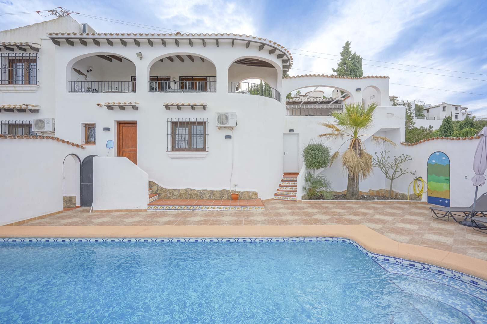 Vue de la façade principale de la villa avec piscine, terrasse carrelée et aménagement paysager.