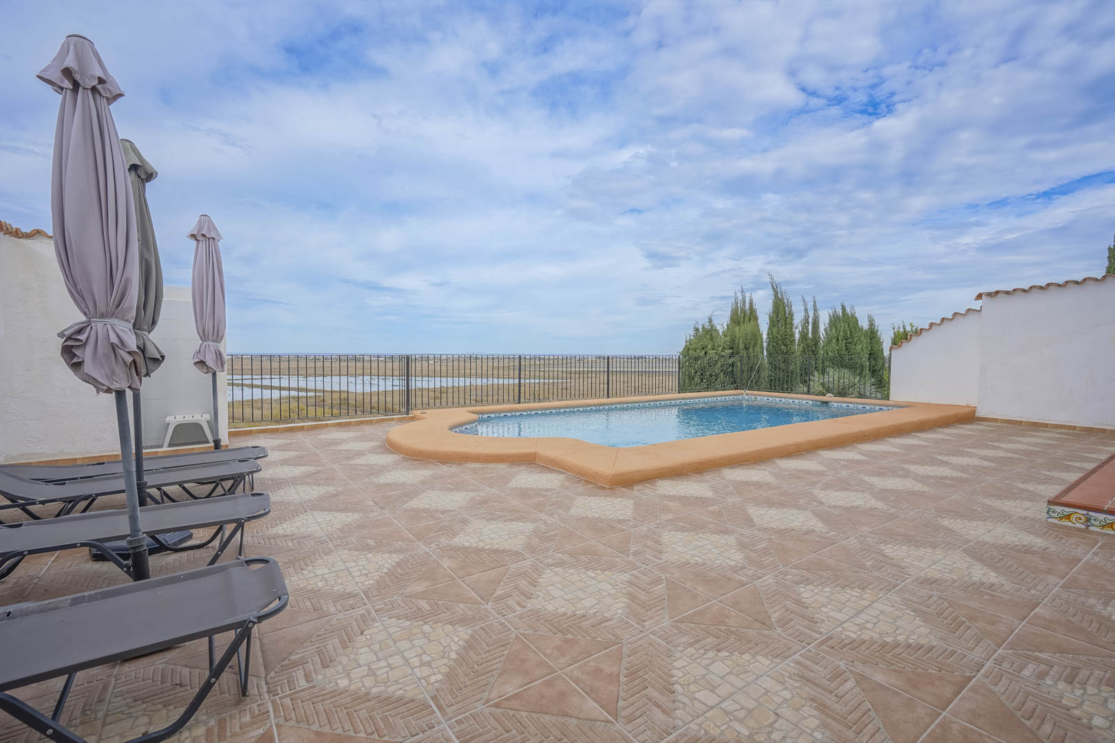 Vue de la piscine avec chaises longues et parasols fermés, donnant sur la réserve naturelle.