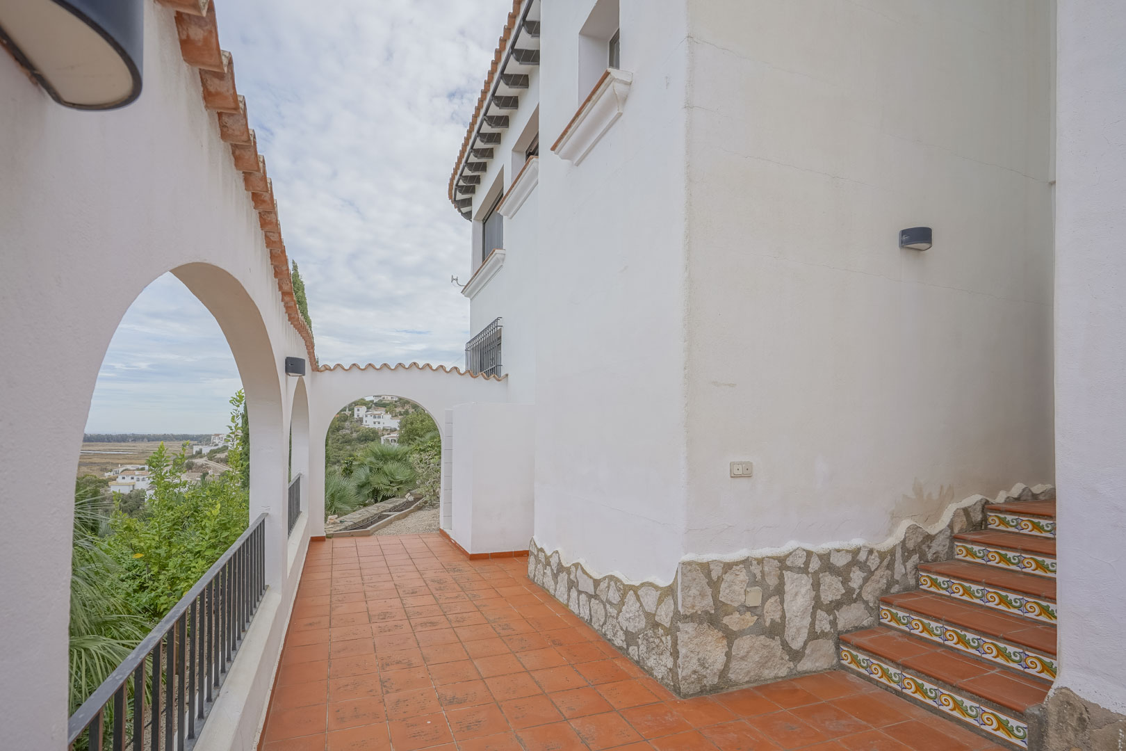 Vue extérieure de la villa avec arches de style espagnol, terrasse en terre cuite et escaliers décoratifs.