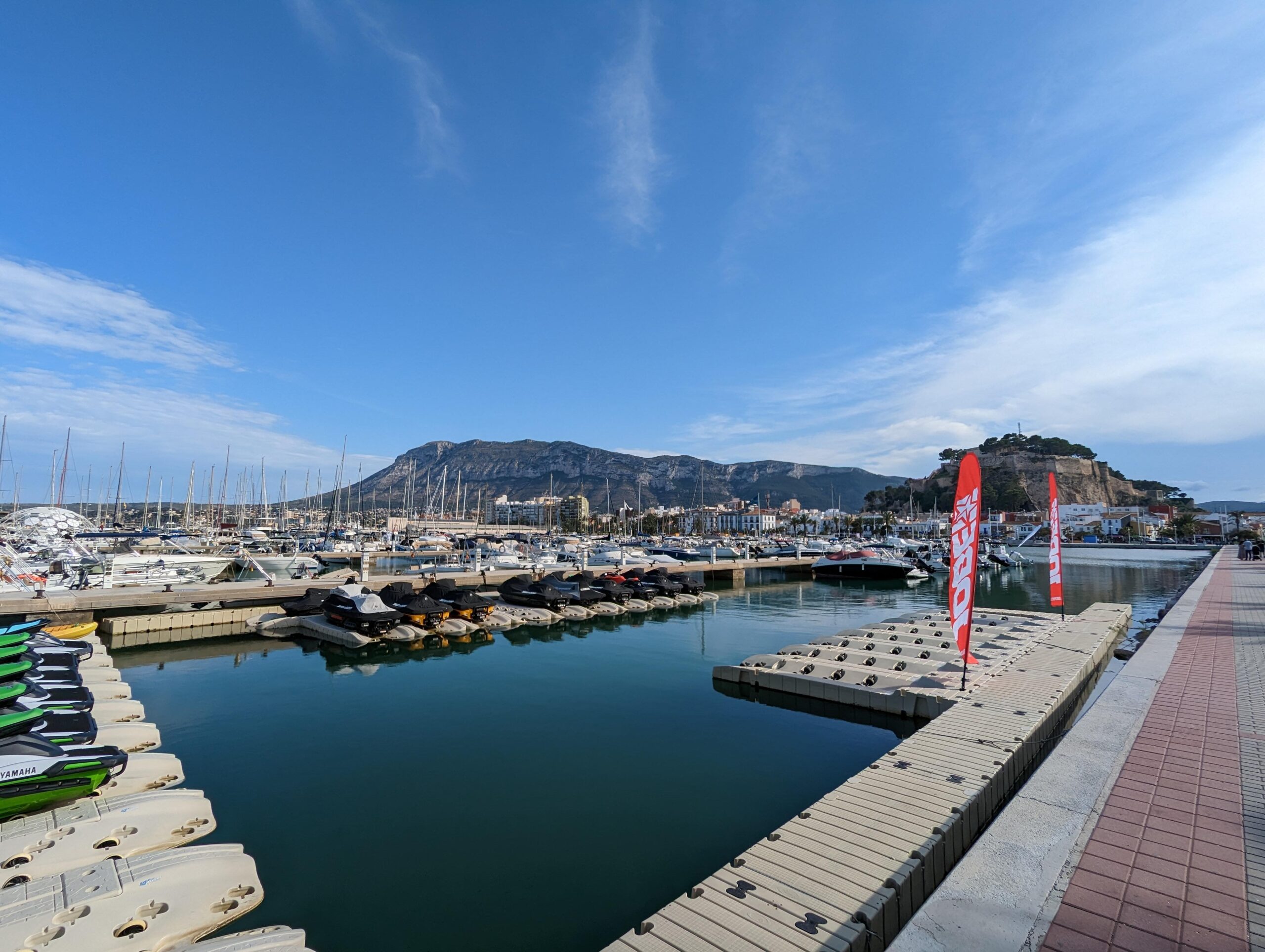 Vue sur la marina avec des jet-skis et des yachts, avec une montagne en arrière-plan.