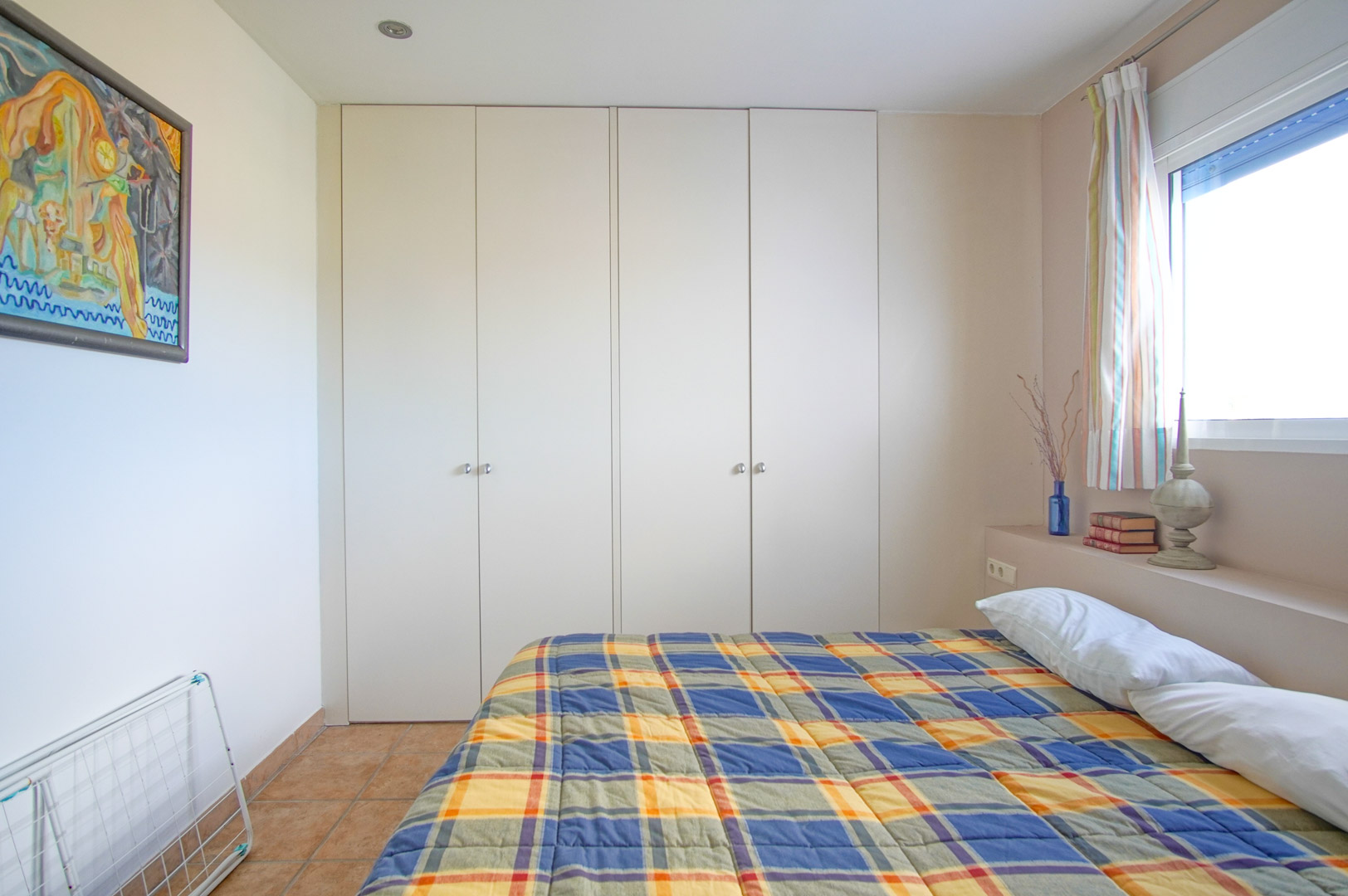 Chambre lumineuse avec de grands placards intégrés blancs, un sol en grès rustique et une fenêtre latérale offrant une clarté naturelle constante.